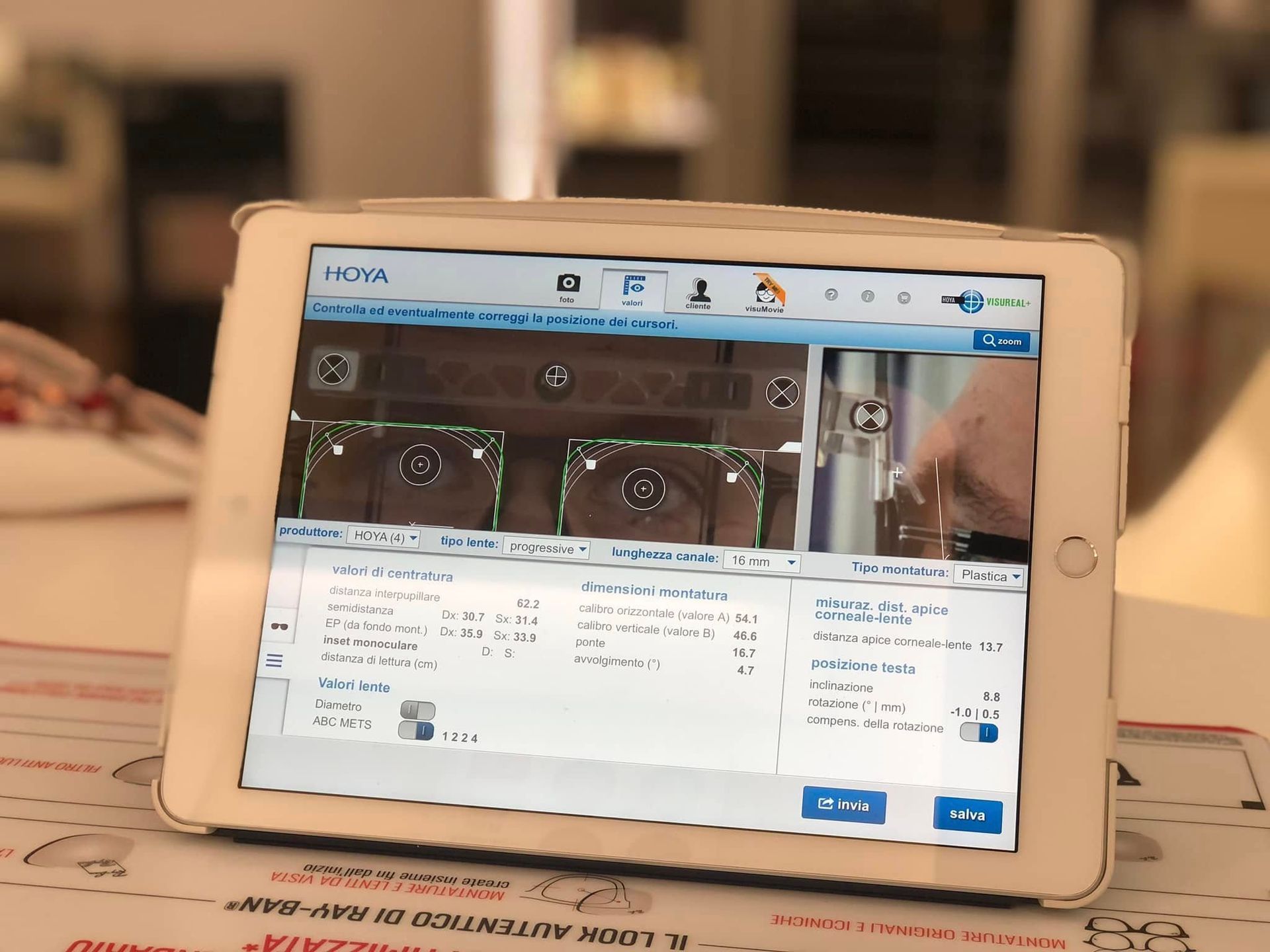 In un ambiente interno sfocato, un tablet bianco mostra una videochiamata e l'interfaccia di un'app su una scrivania.
