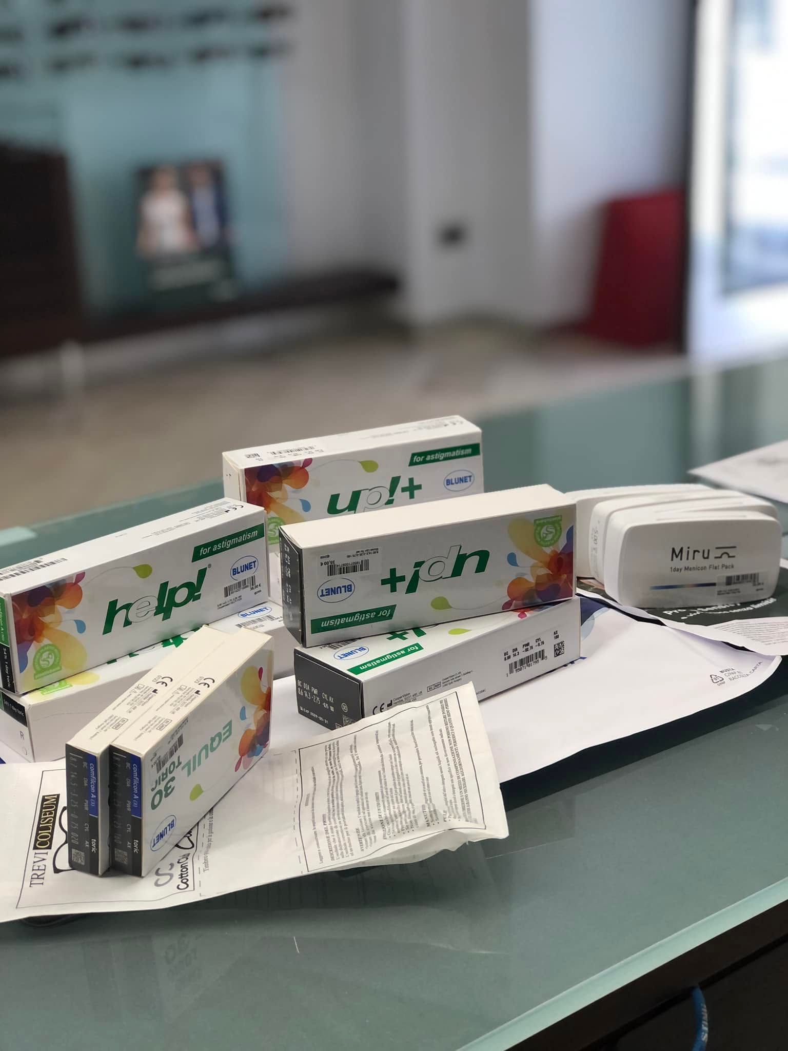 Scatole di medicinali e una bottiglia su un tavolo di vetro con un foglietto illustrativo piegato e una striscia di carta.