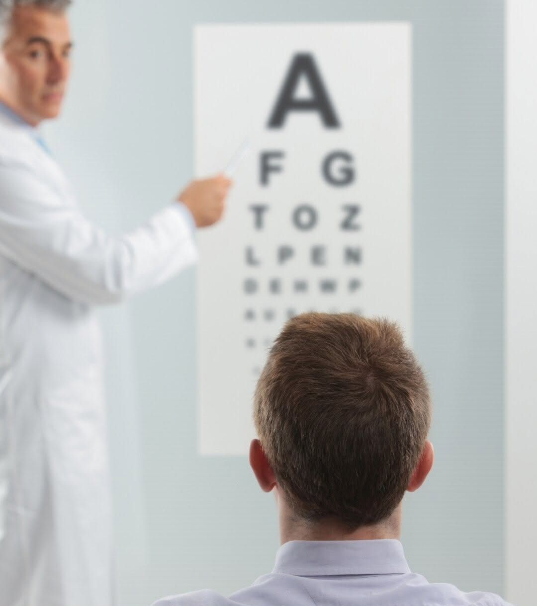 Esame della vista con tabella optometrica, con il medico che la indica mentre il paziente è seduto di fronte alla tabella.