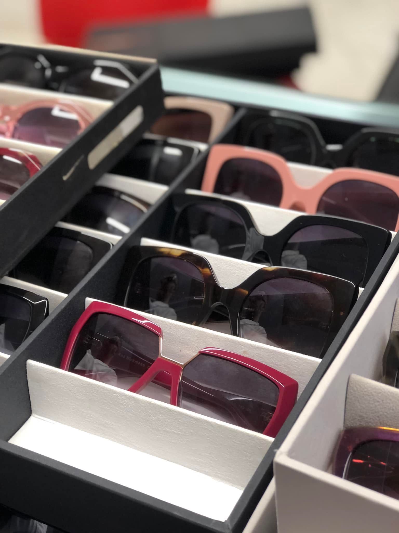 Occhiali da sole esposti in scatole aperte, con montature nei colori nero, rosa e rosso.