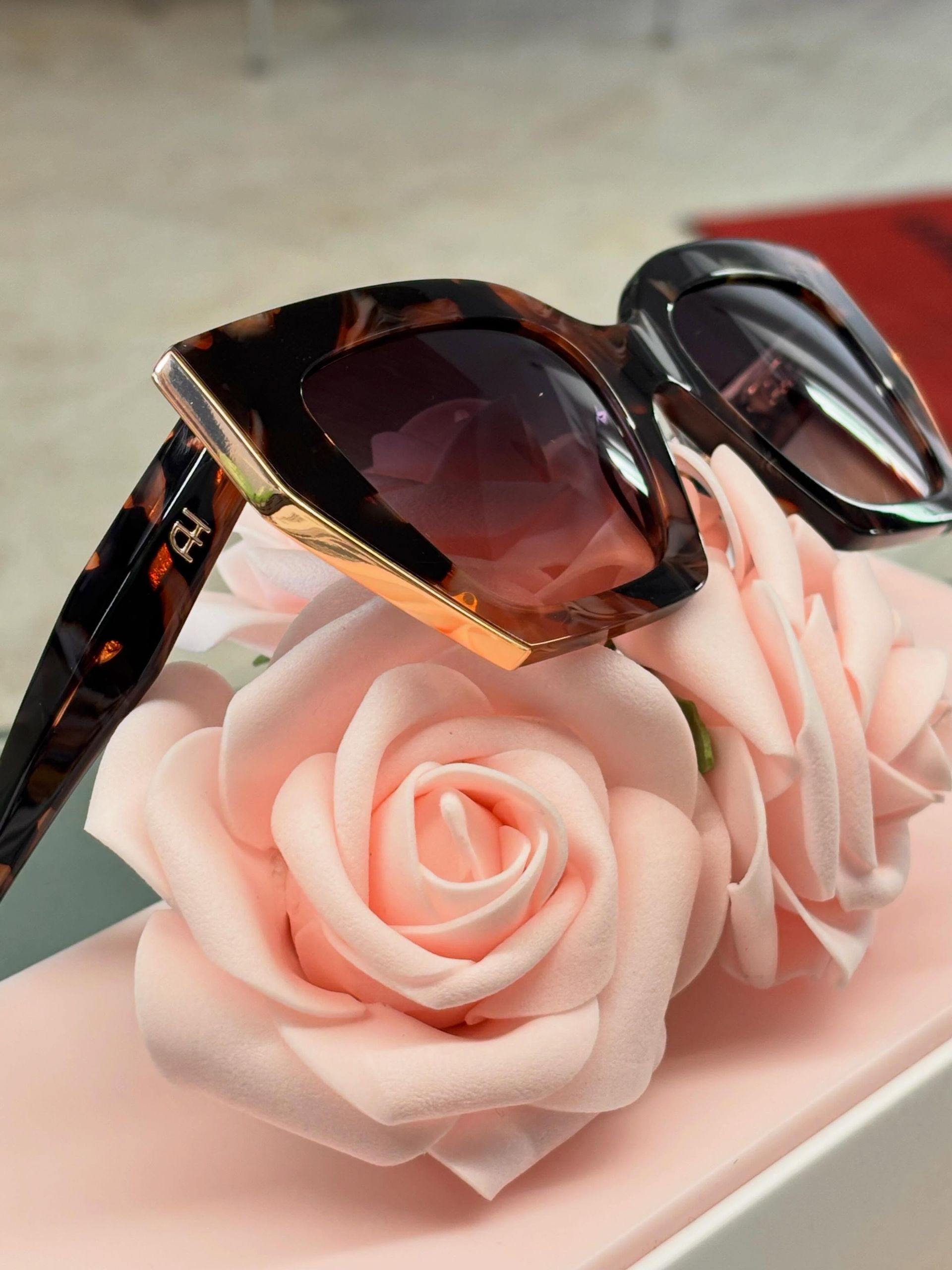 Occhiali da sole appoggiati su fiori rosa a forma di rosa su un vassoio bianco.
