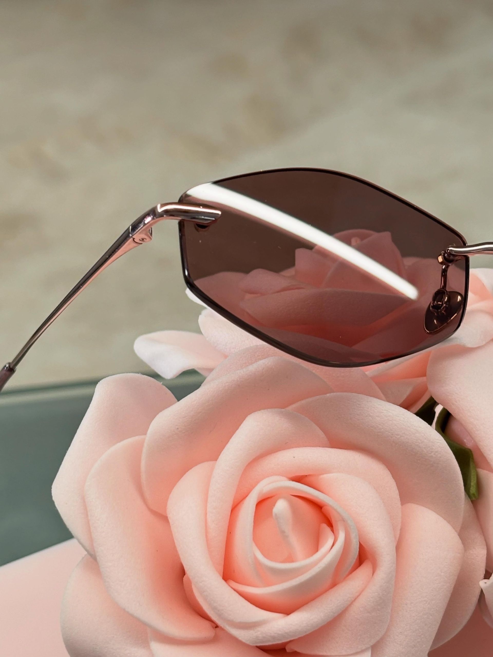 Occhiali da sole rosa appoggiati su un bocciolo di rosa rosa pallido