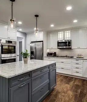 Modern white kitchen with large gray island, stainless appliances, pendant lights, and wood floors