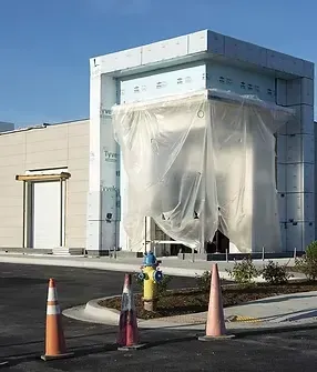 Building under construction wrapped in white plastic, with traffic cones and a hydrant in front