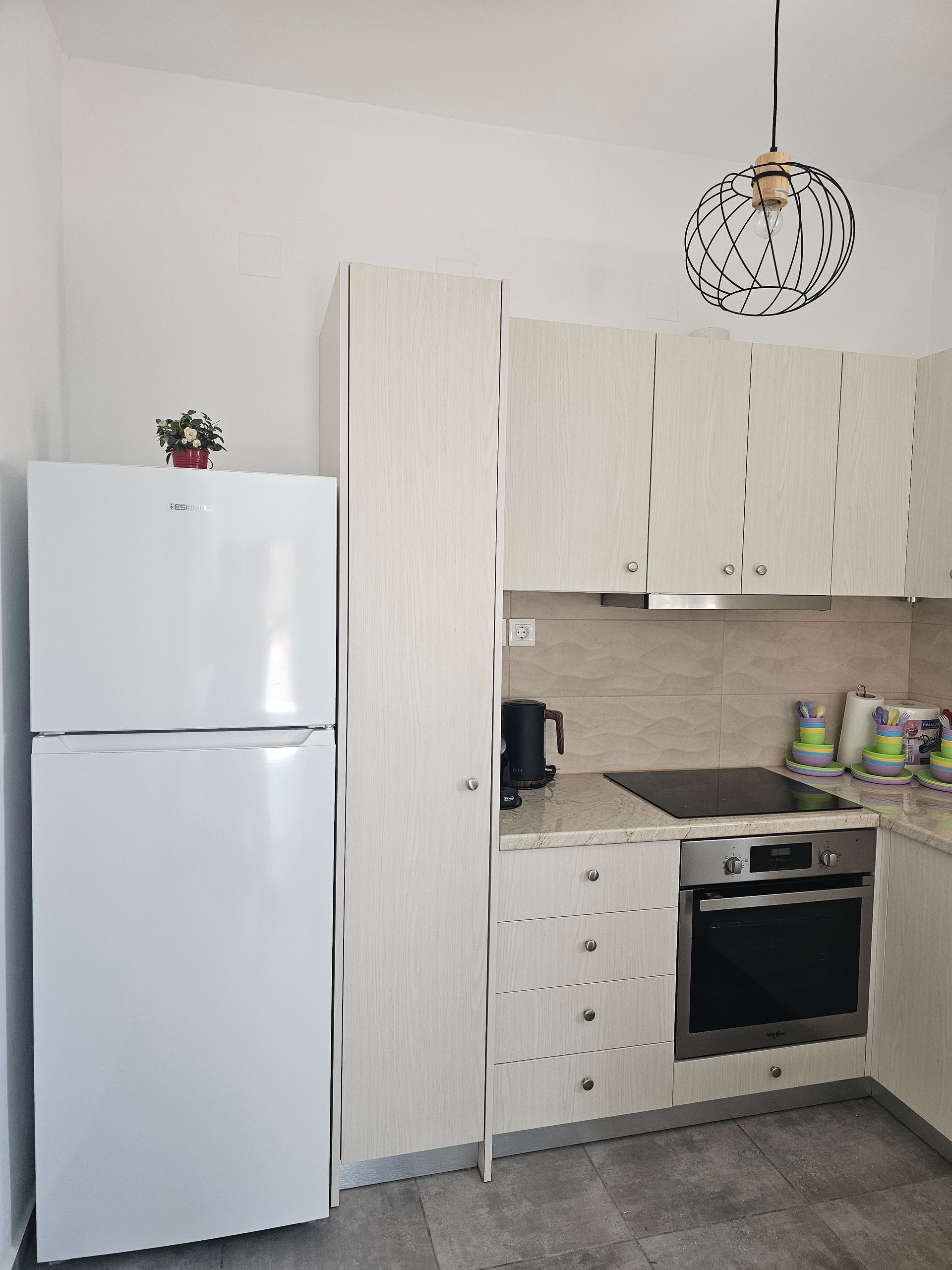 Small white kitchen with refrigerator, cabinets, oven, and patterned ceiling light.