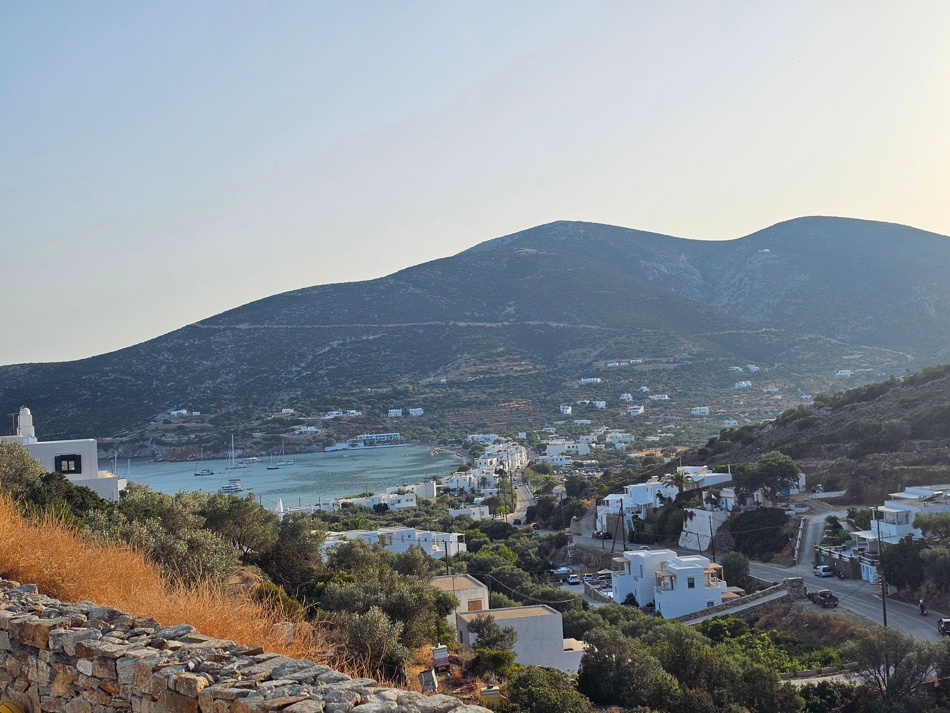 Coastal hillside town at dusk with mountains, bay, and white houses below