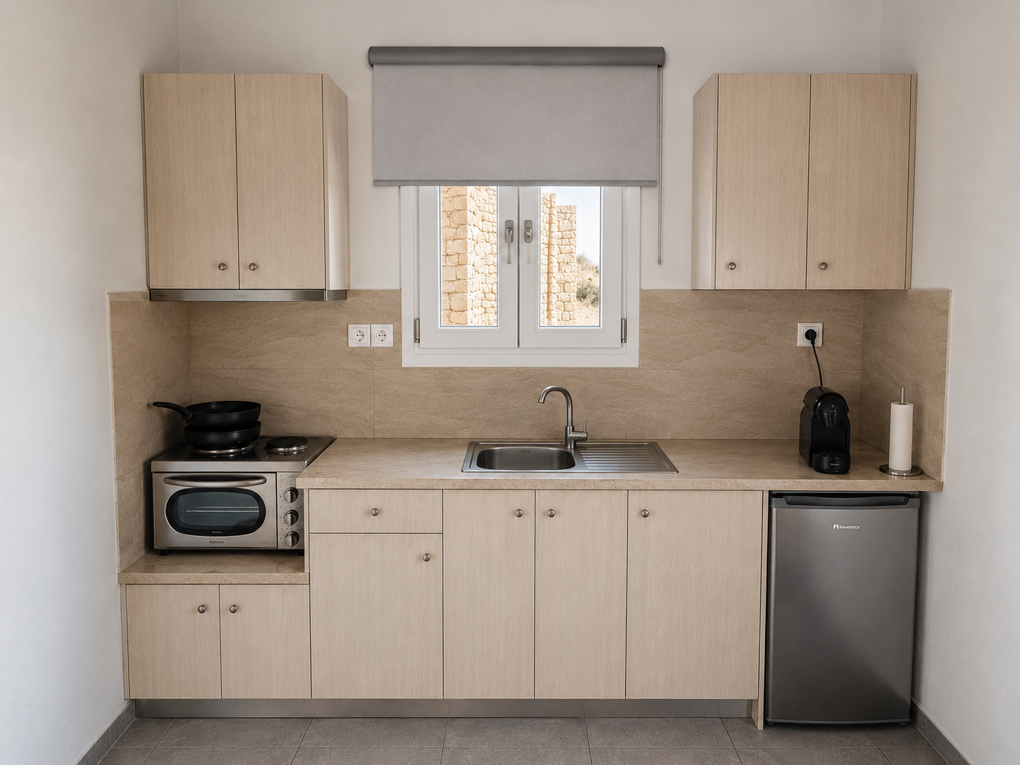 Compact beige kitchen with sink, window, stove, and mini fridge under cabinets