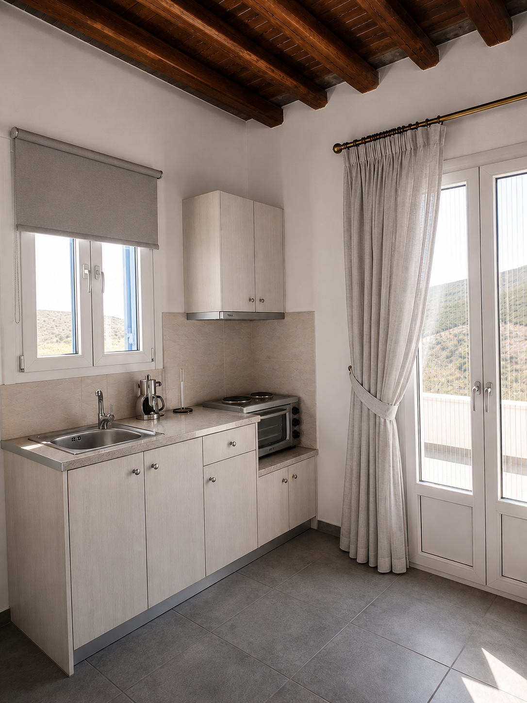 Small white kitchen with sink, cabinets, oven, window, and French doors under a wood-beamed ceiling.