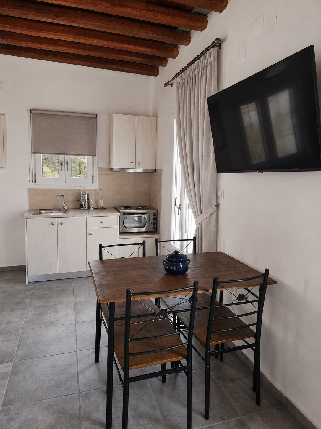 Small kitchen-dining area with wooden table, chairs, white cabinets, and a wall-mounted TV.
