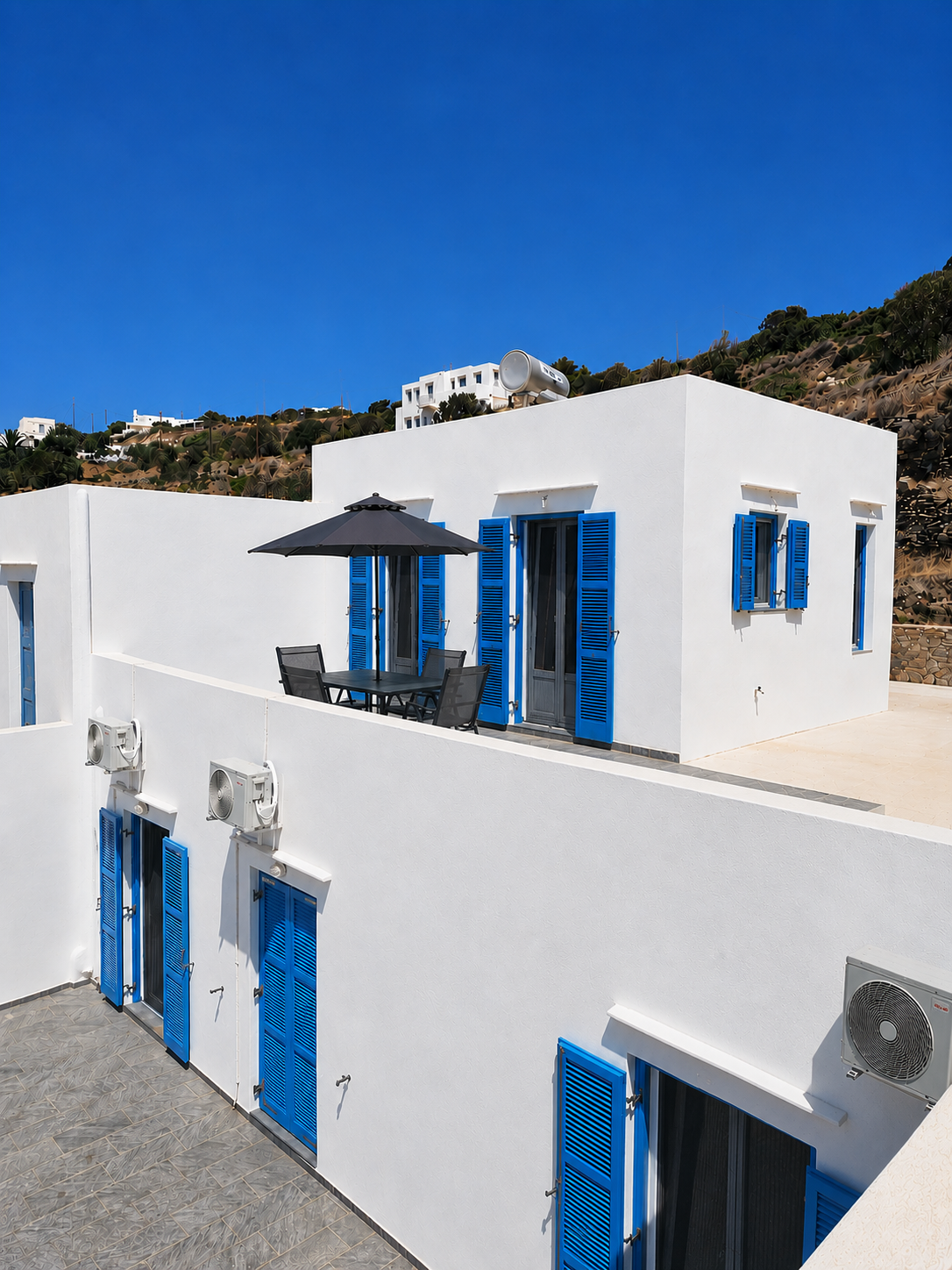 White Mediterranean-style building with bright blue shutters and balcony under a clear blue sky