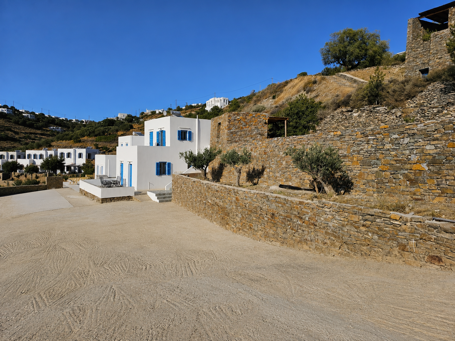 White building beside stone wall on a gravel lot under a bright blue sky