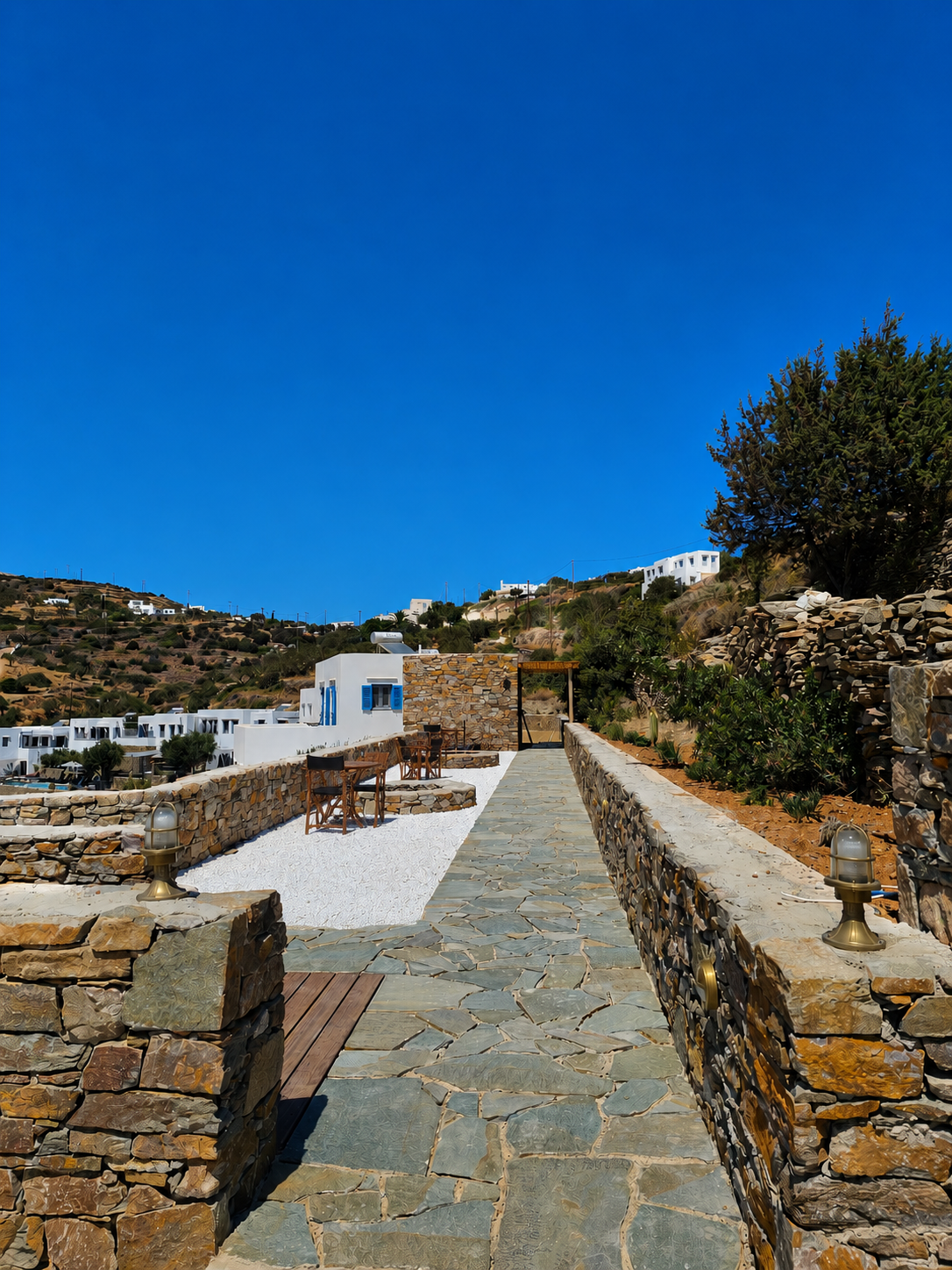 Stone walkway beside white houses on a rocky hillside under a clear blue sky