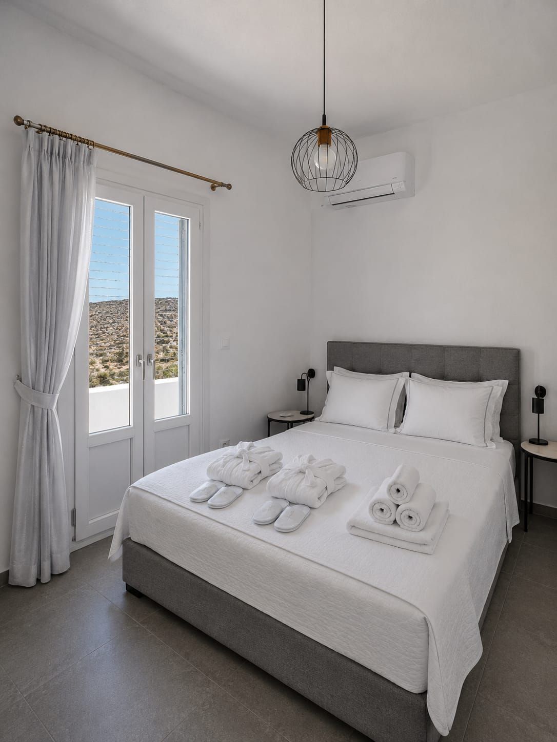 Bright white bedroom with a gray bed, balcony doors, and a modern light fixture