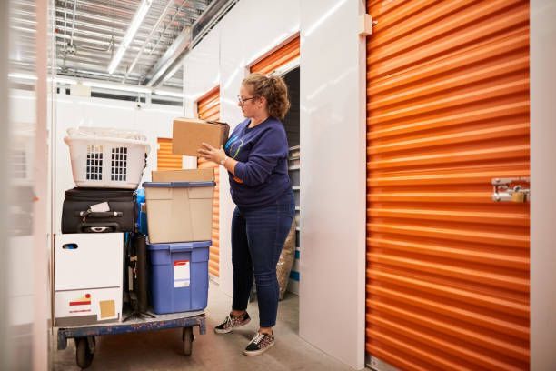 Woman organizing boxes in self storage units with secure orange doors and metal interior.