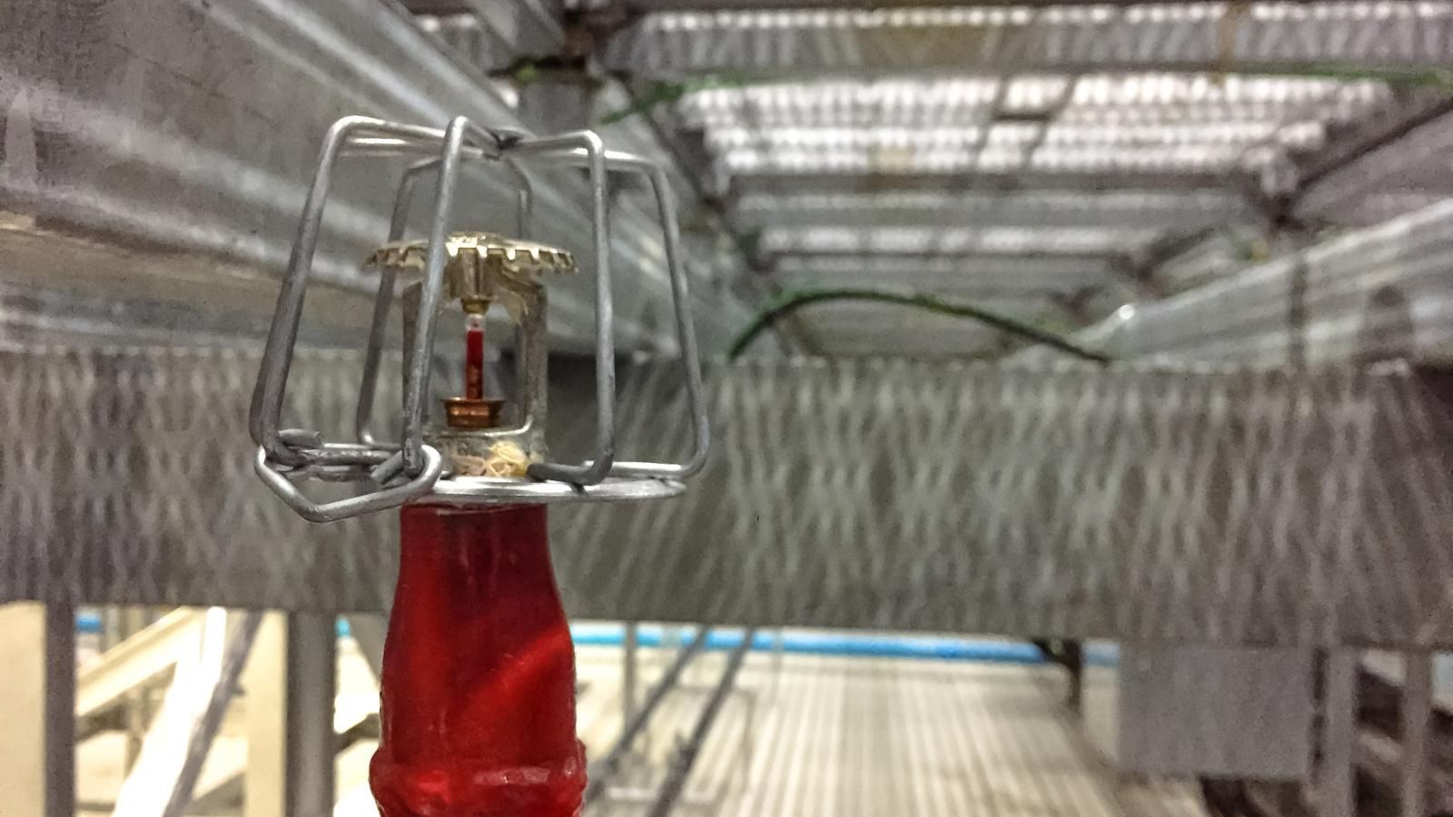 fire suppression systems Close-up of a mechanical device with red base in front of a blurred metal walkway or grid structure