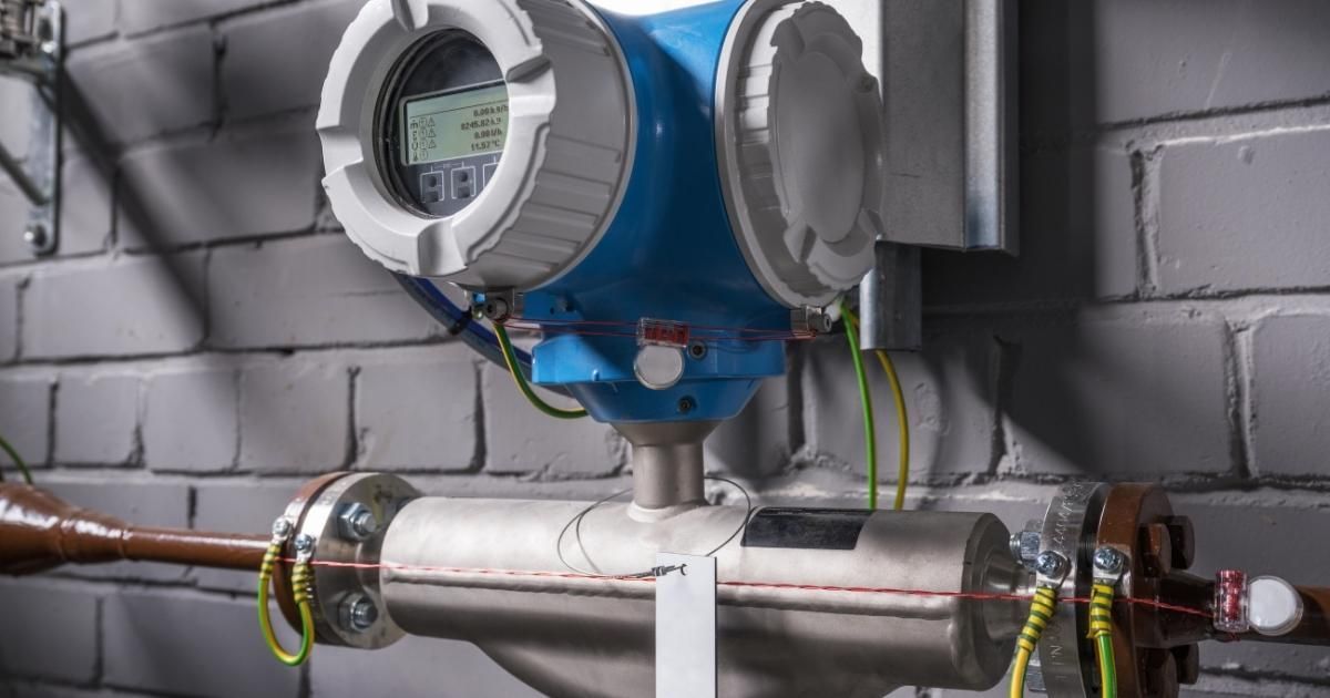 Blue and white industrial flow meter attached to a pipe on a brick wall.
