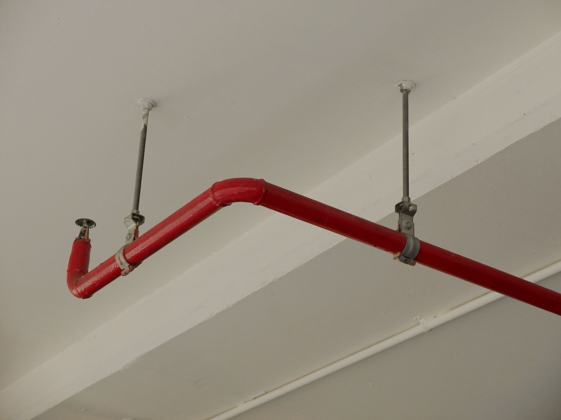 Red fire sprinkler pipe suspended from a ceiling with metal rods