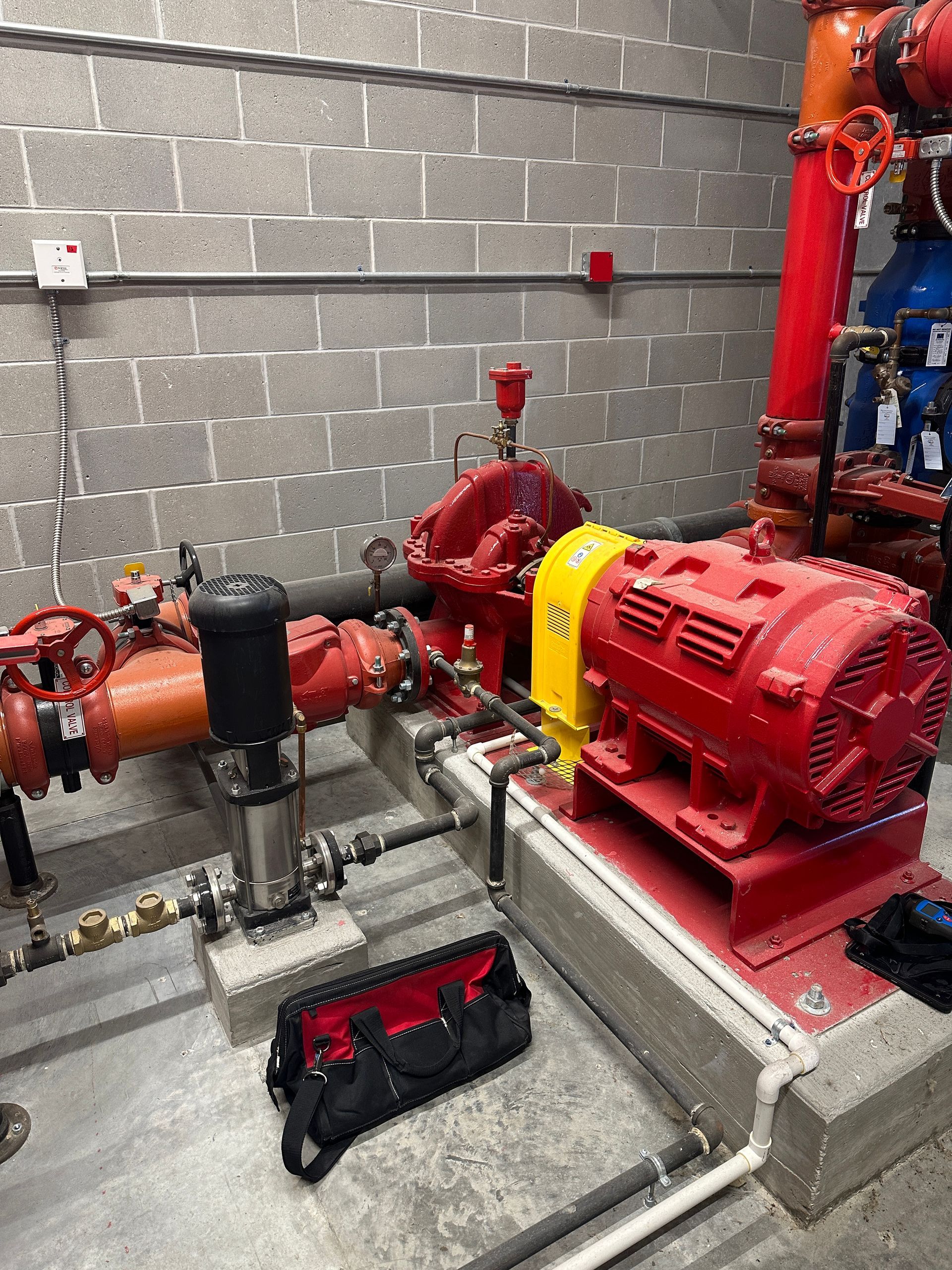 A red pump is sitting in a room next to a brick wall.