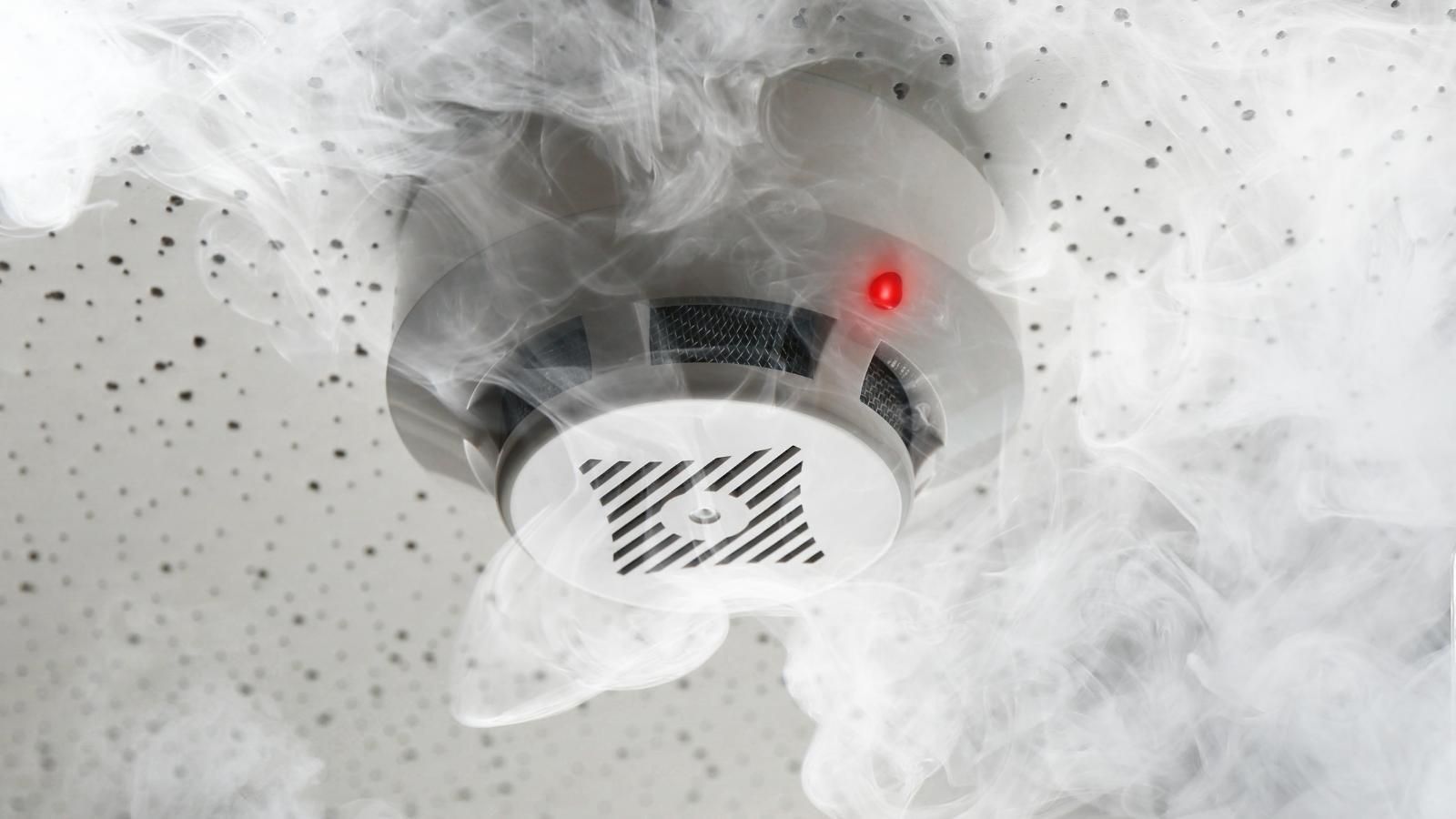 Smoke billowing around a fire alarm with a lit red indicator.