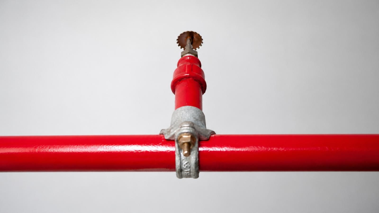 sprinkler piping system Red pipe with a metal clamp and a small red-topped fitting against a white background