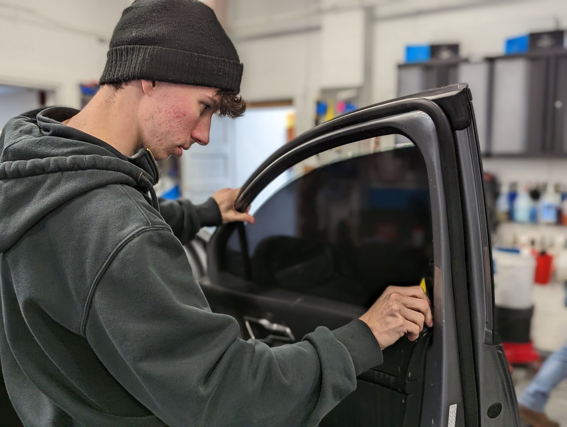 a man is installing window tinting on a car in a garage .a blue bmw m2 is driving on a snowy road .  Ceramic coating, PPF, Tint, Vinyl Wrap, johnstown pa www.mdxdetailing.com