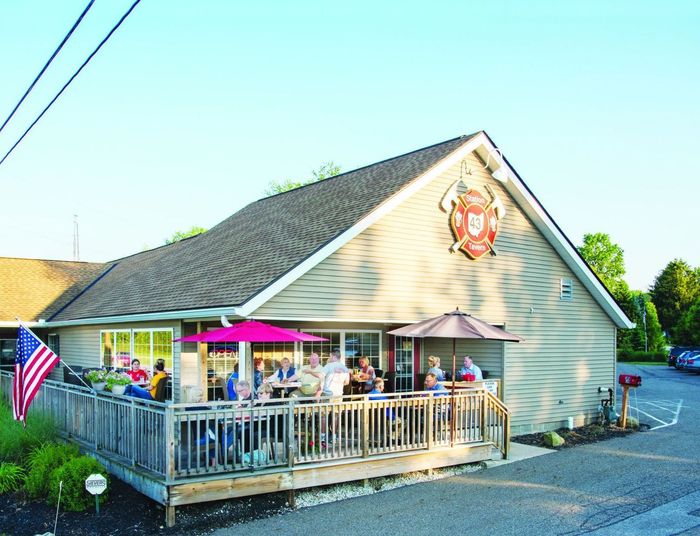 Restaurant with outdoor patio, people seated at tables under umbrellas. American flag visible.