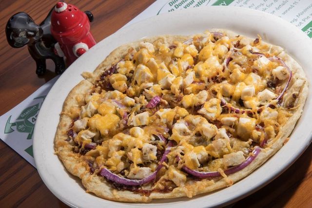 BBQ chicken flatbread pizza with red onion and cheddar cheese on a plate.