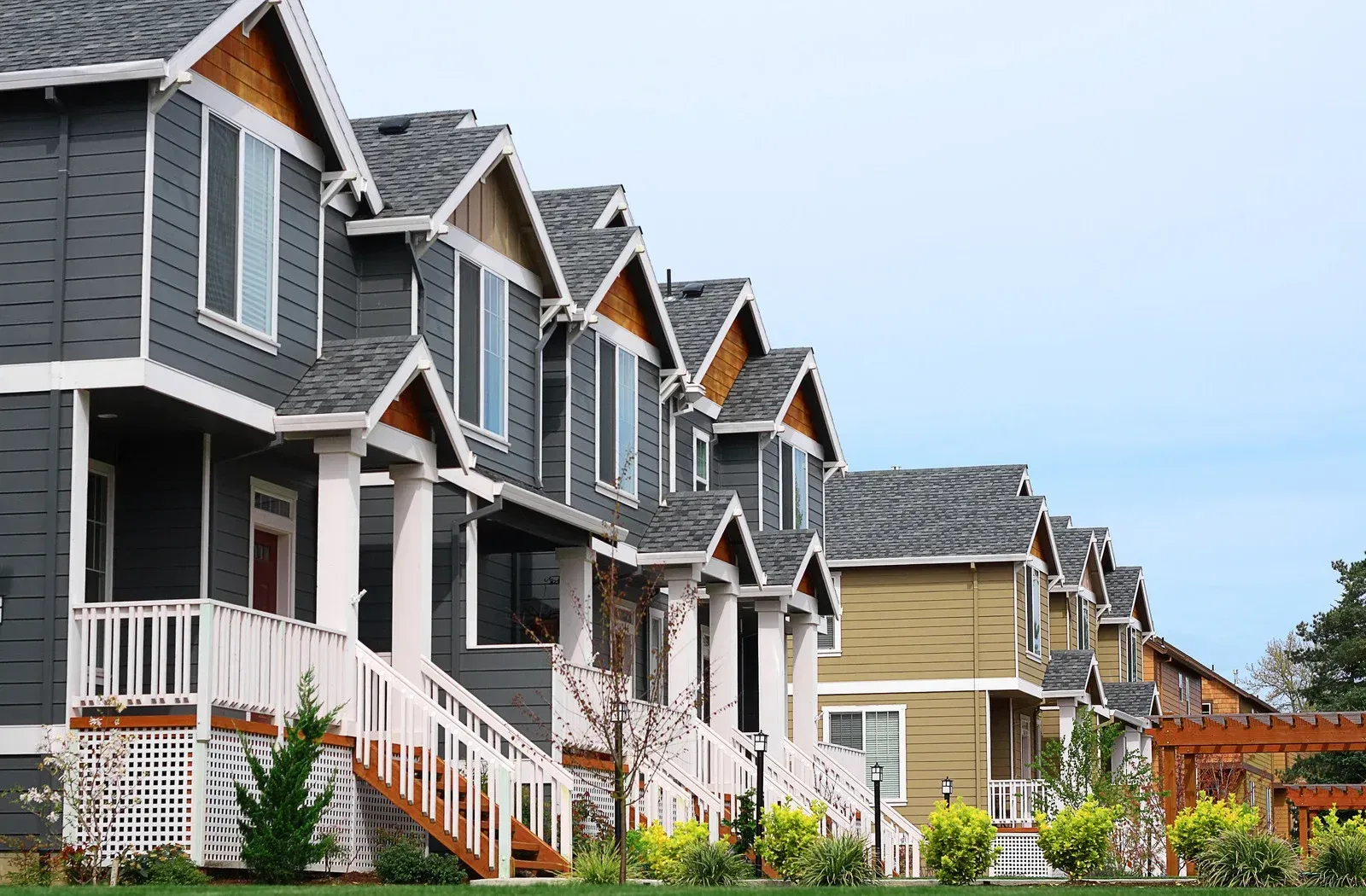 Row of townhouses with gray and tan siding, white trim, and small front porches under a cloudy sky.