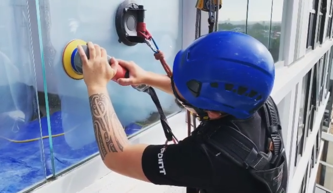 Worker in a blue helmet sanding a window with a power sander on a building exterior