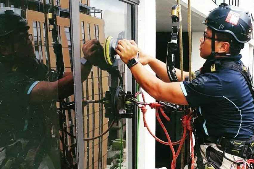 Rope worker in helmet securing window opening beside reflective glass facade
