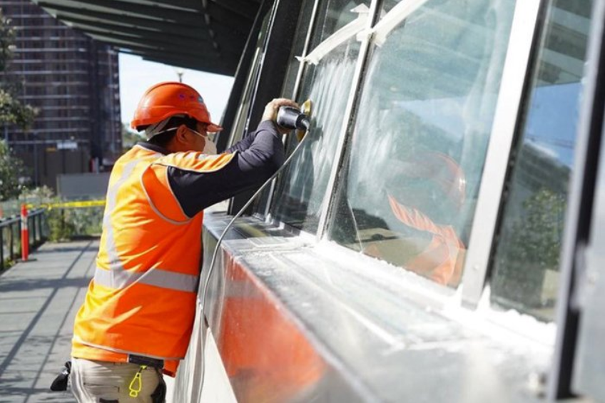 Worker in orange safety vest cleaning a large glass storefront window outdoors