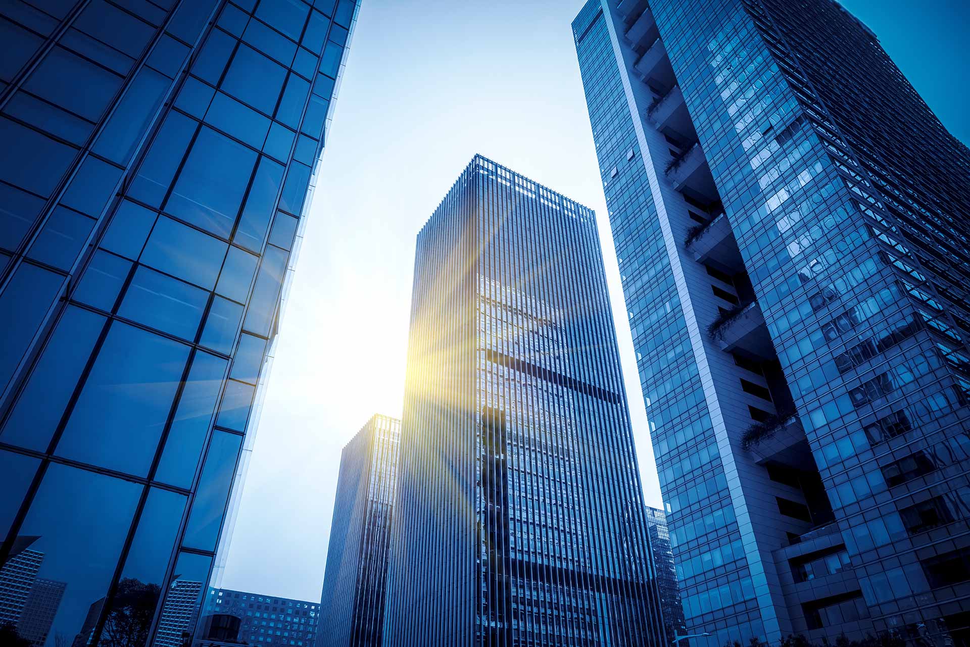 Sunlit blue glass skyscrapers viewed from below against a clear sky