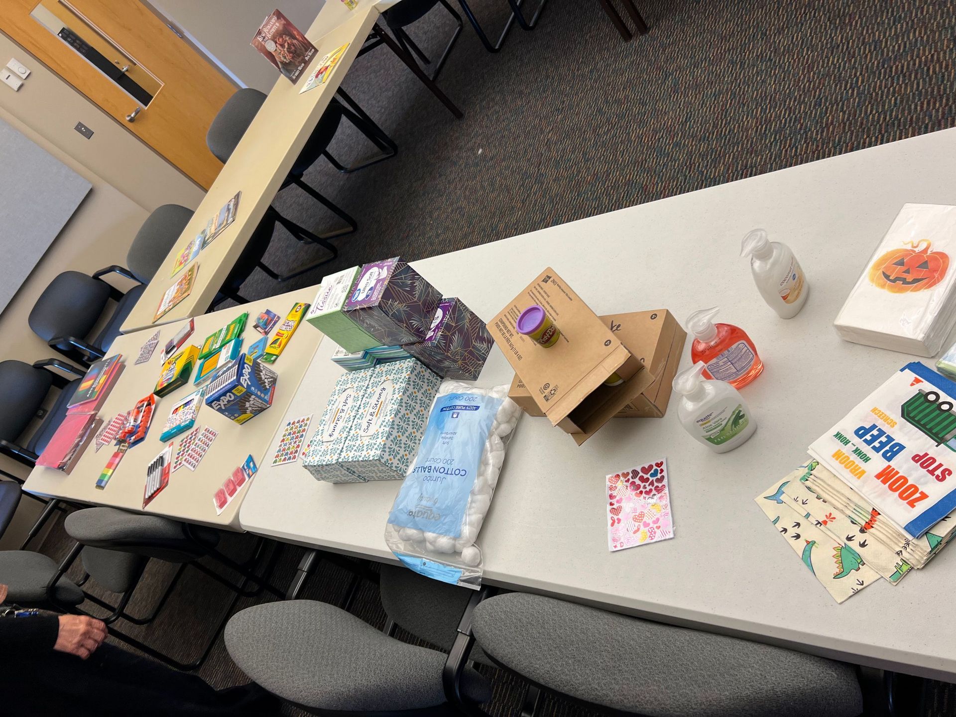 Craft projects on a long white table, including boxes, cards, and bottles, in a brightly lit room.