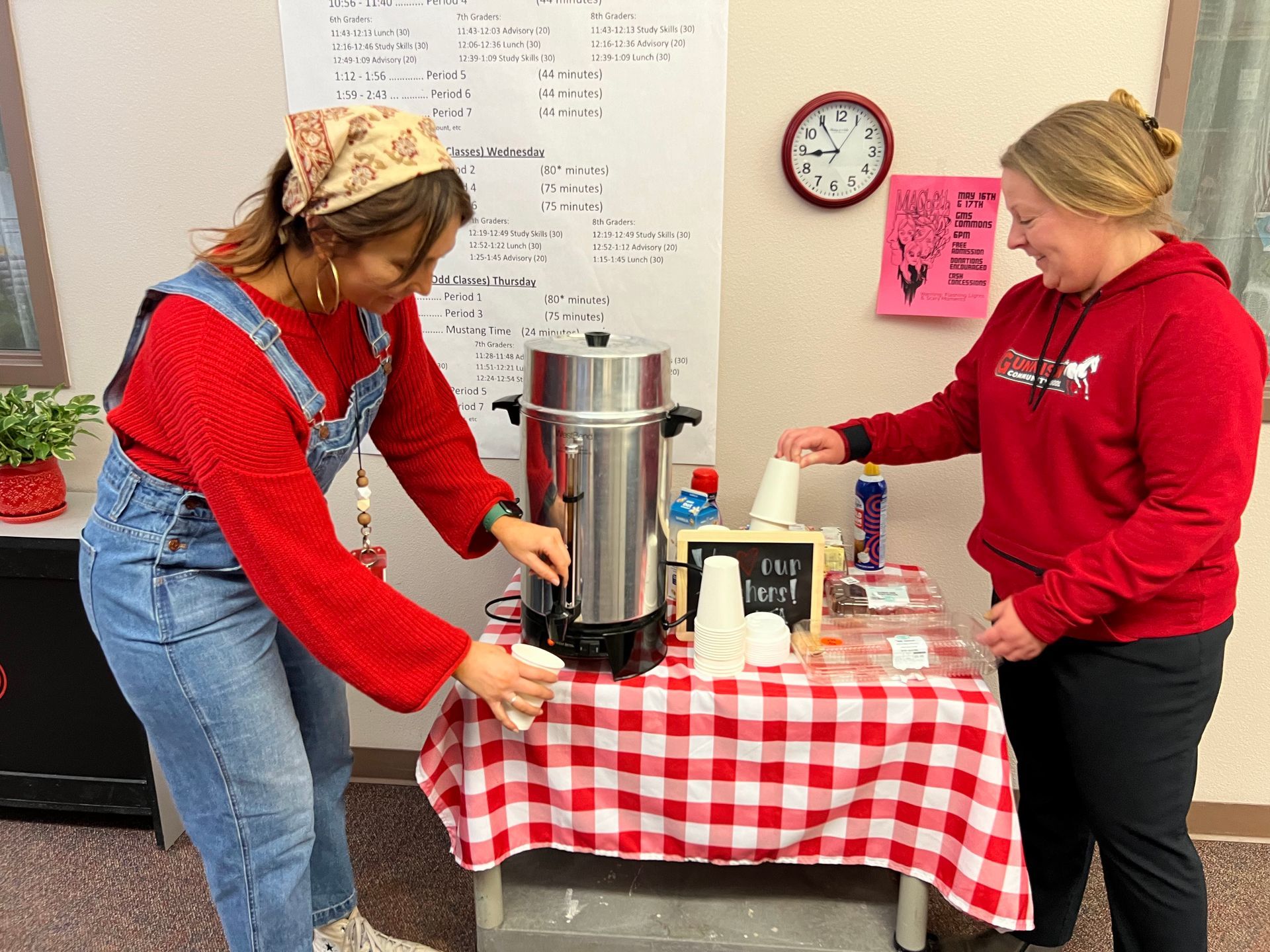 Two people by a coffee station. One pours from a large urn; the other grabs a cup.