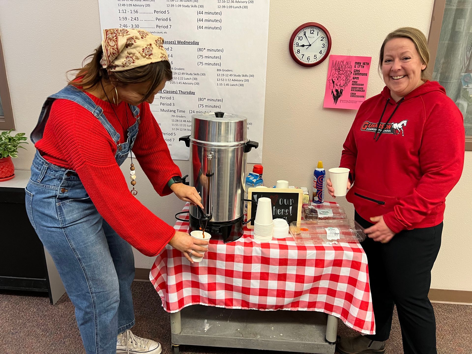 Two people serving coffee at a table covered in red and white checkered fabric. One pours from a coffee urn.