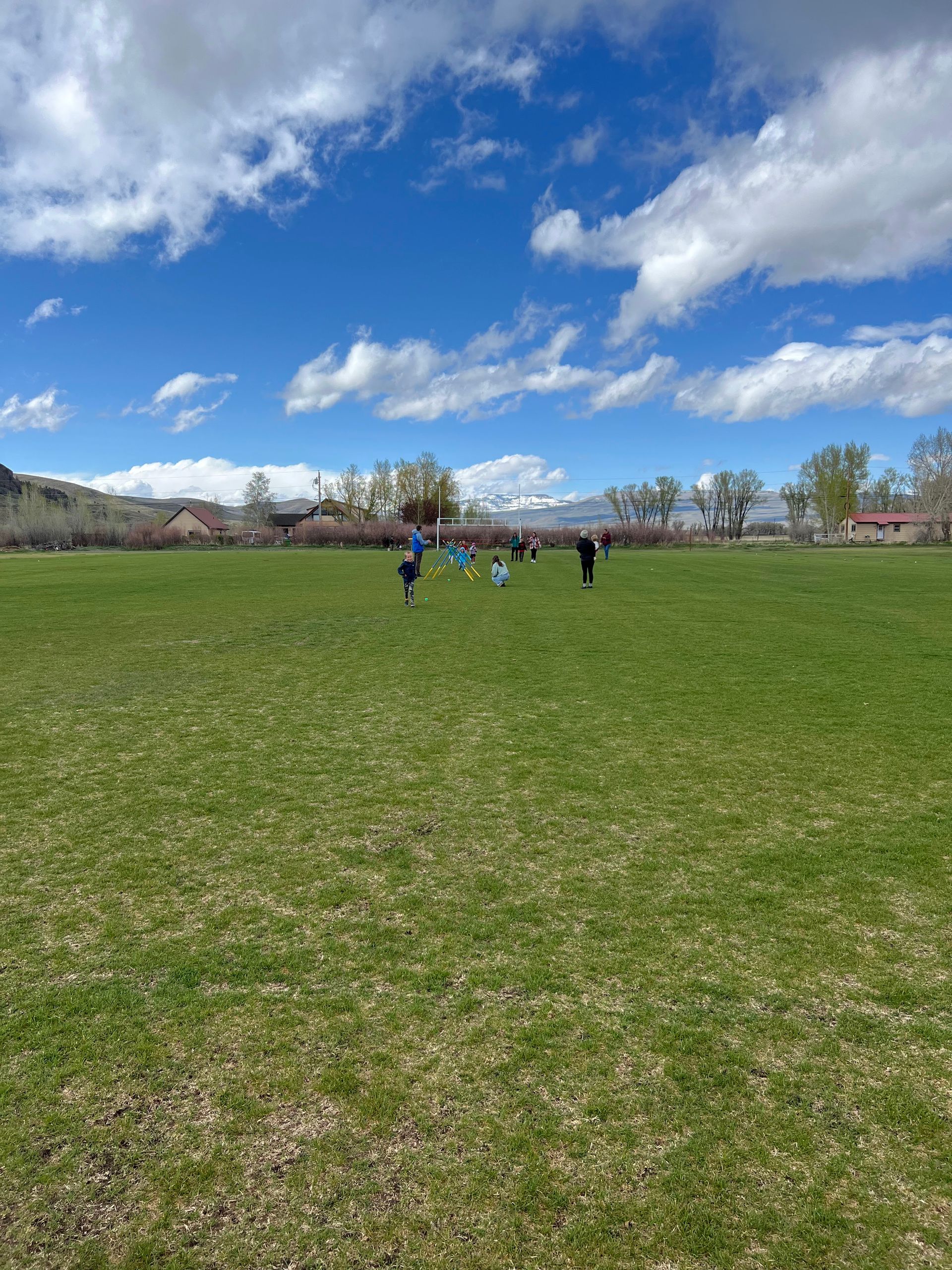 Green field with children playing soccer under a partly cloudy blue sky.