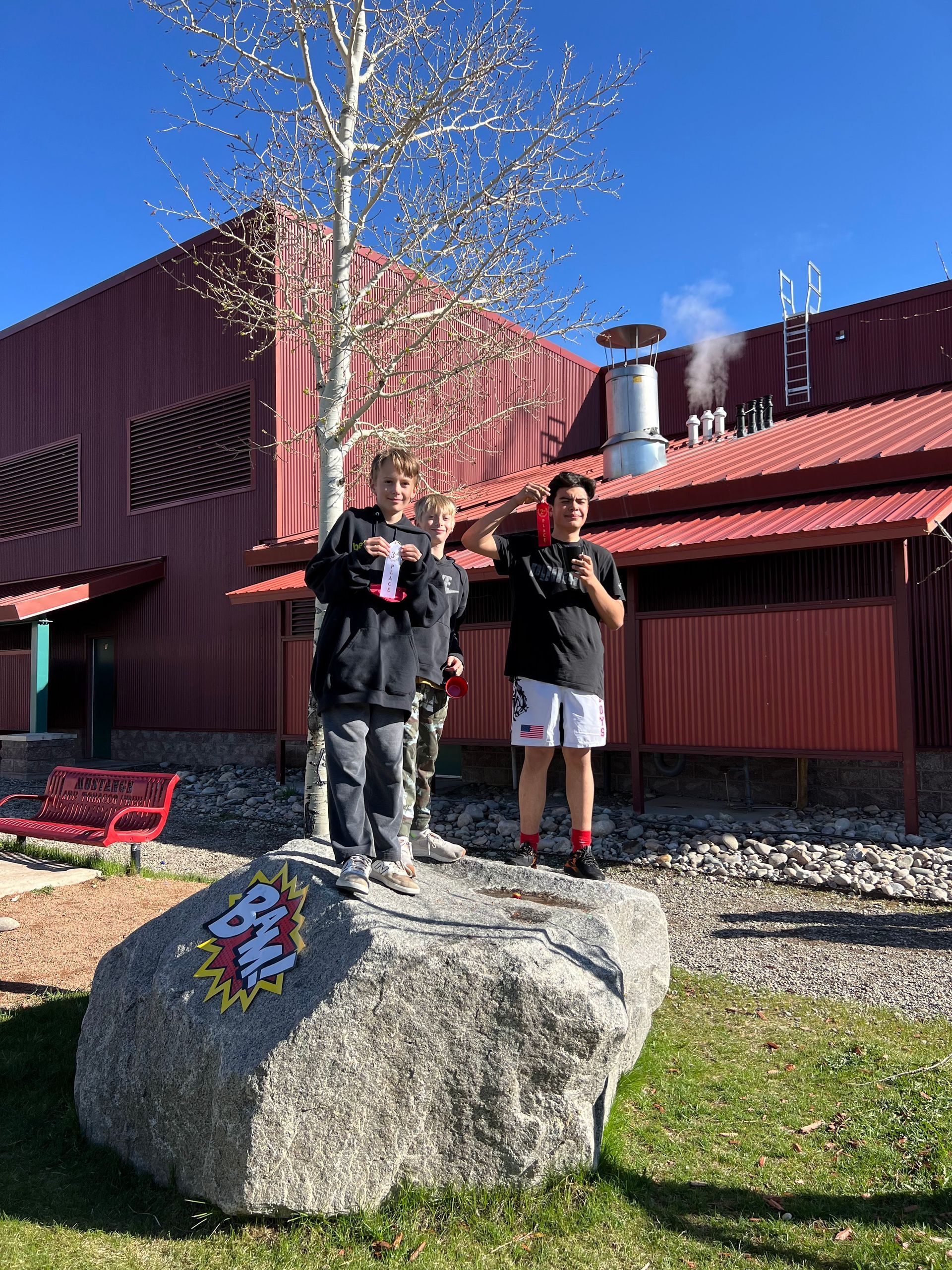 Two people standing on a painted rock in front of a red building with a smokestack.