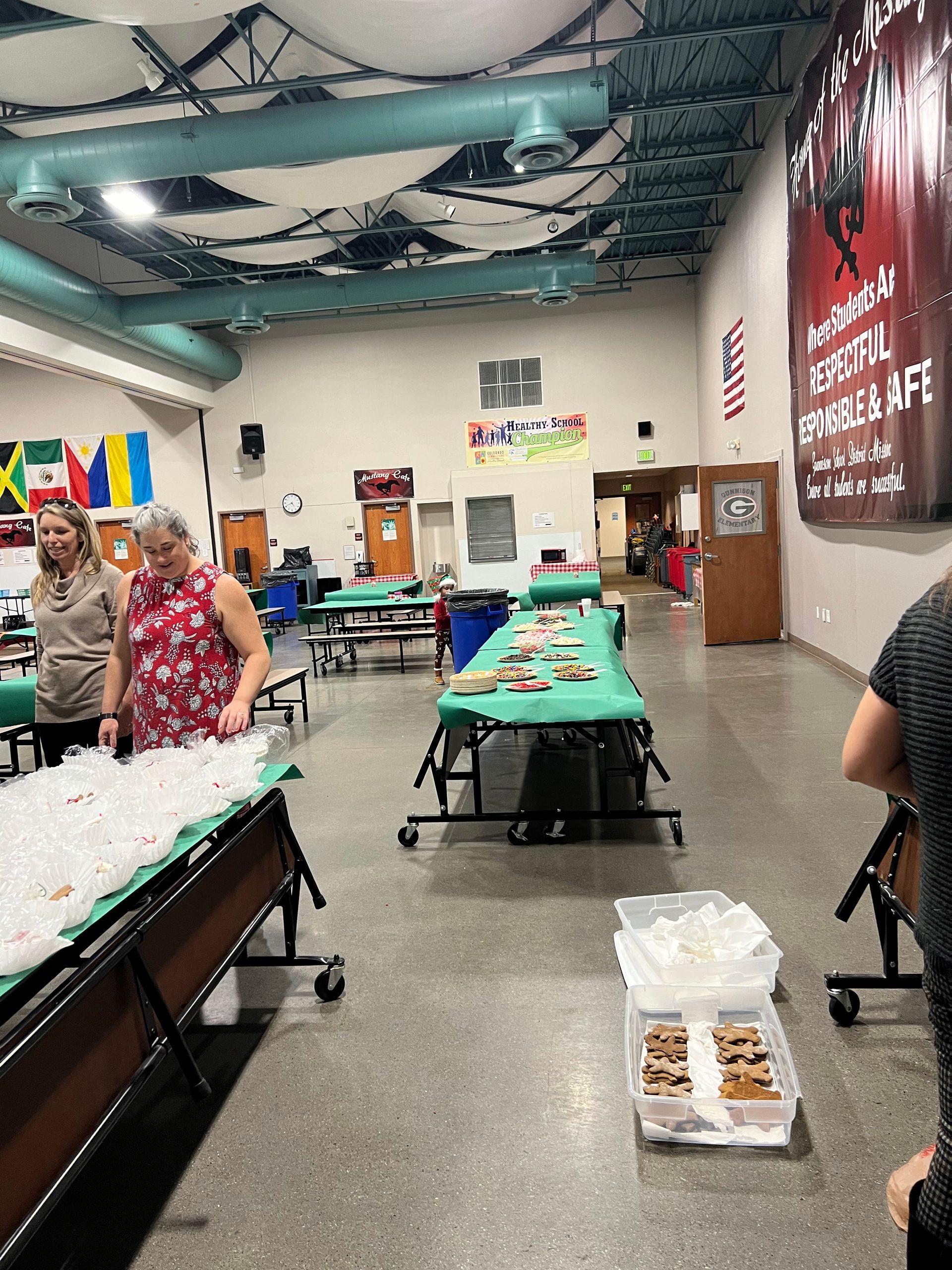 People stand near long tables laden with food in a brightly lit room with flags and a poster.