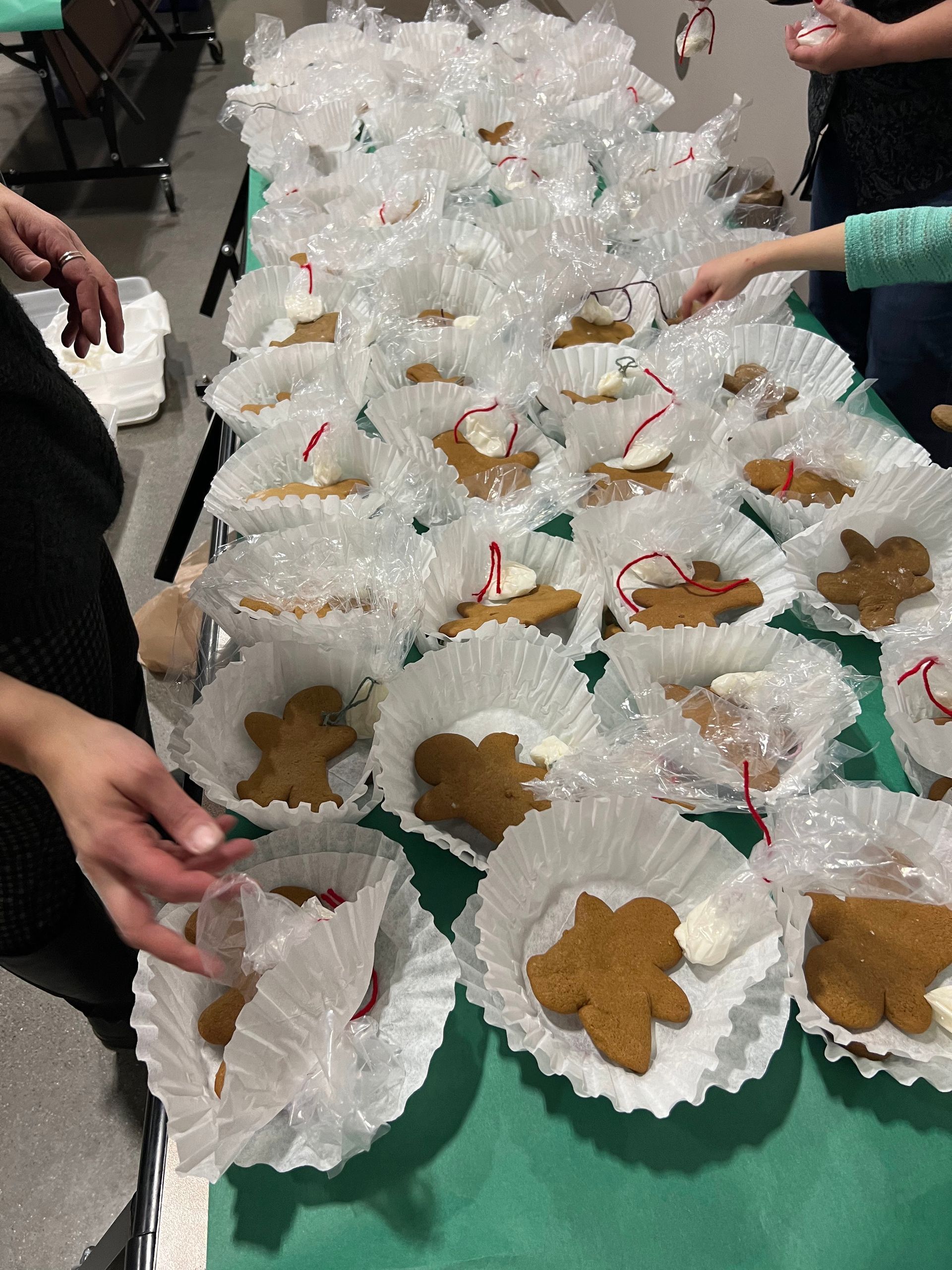 Gingerbread cookies in white paper cups wrapped with plastic, on a green table. People reaching for them.