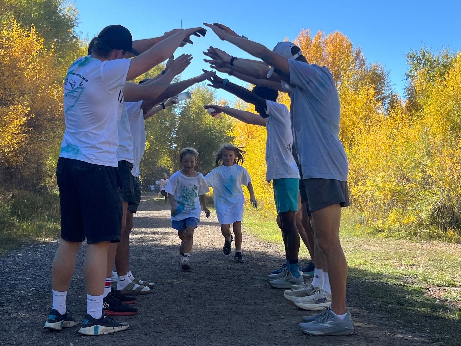 People forming a tunnel for two children running on a path. Autumn foliage in background.