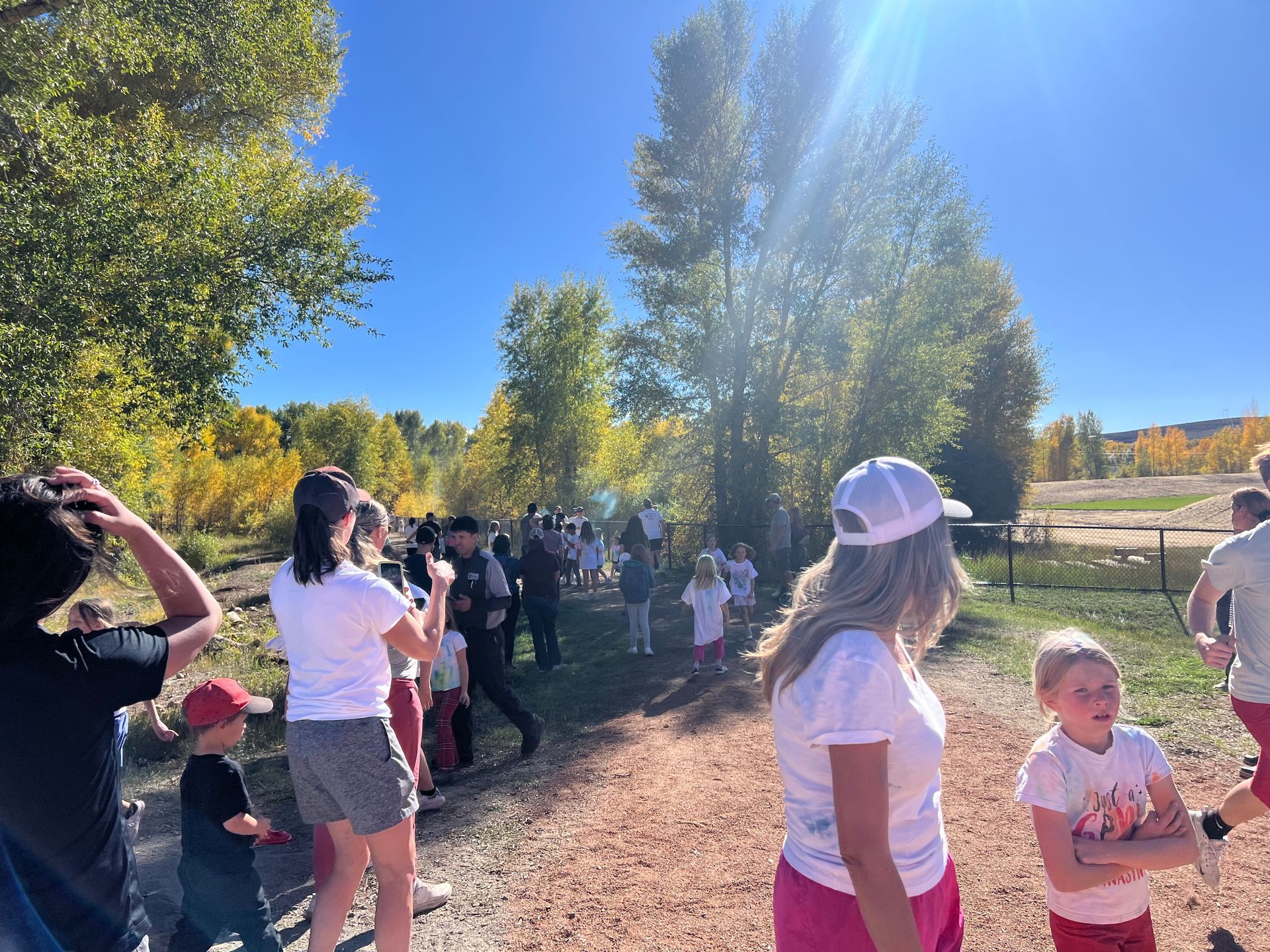 Cross country race on a sunny day. Spectators watch runners on a dirt path with trees.