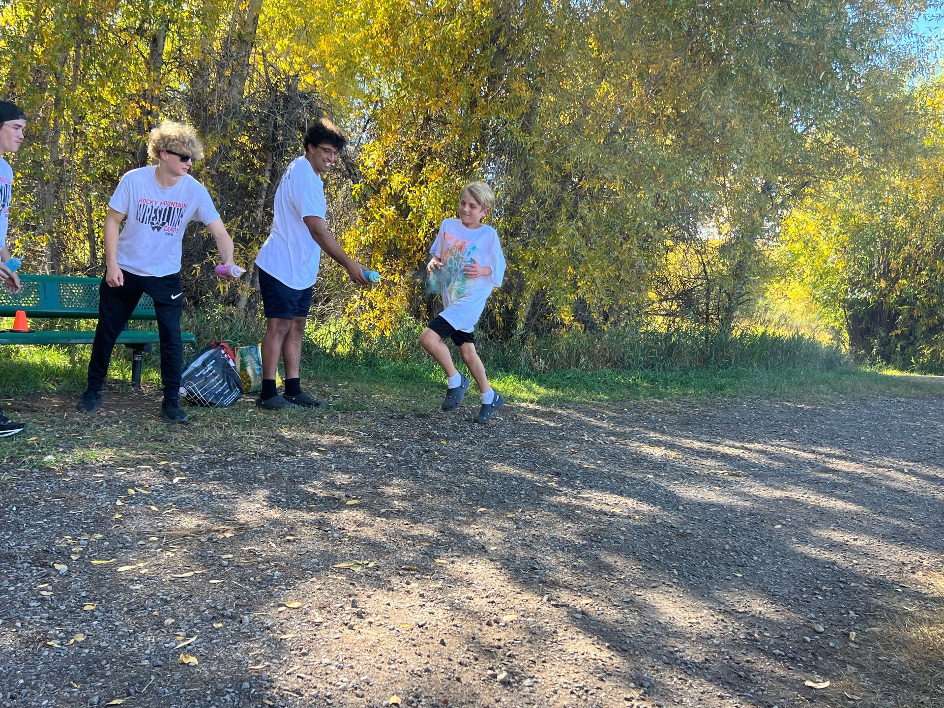 Boys in white shirts pass an object in an outdoor setting with trees.