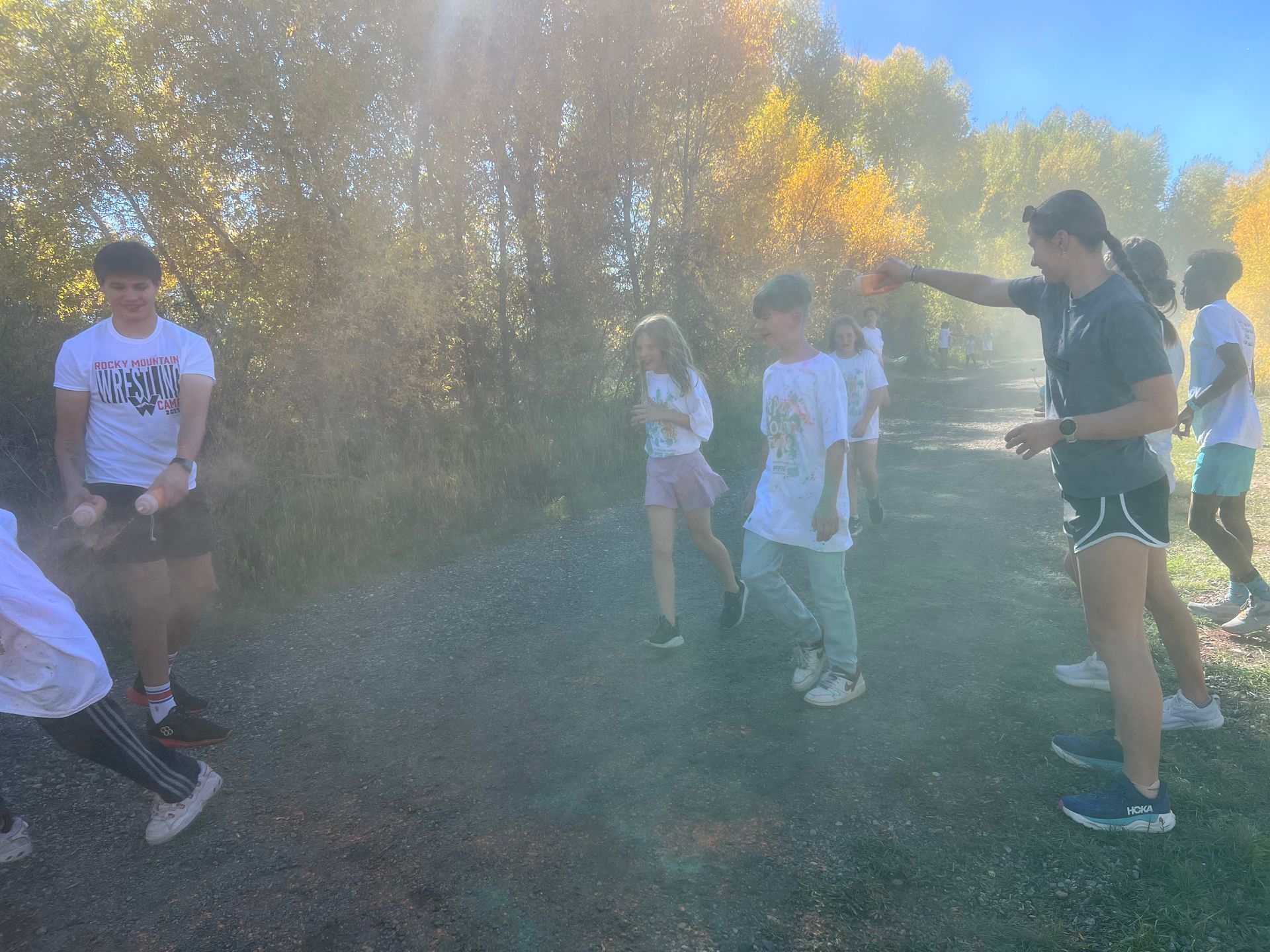 Children running through a cloud of colorful powder outdoors, guided by a coach.