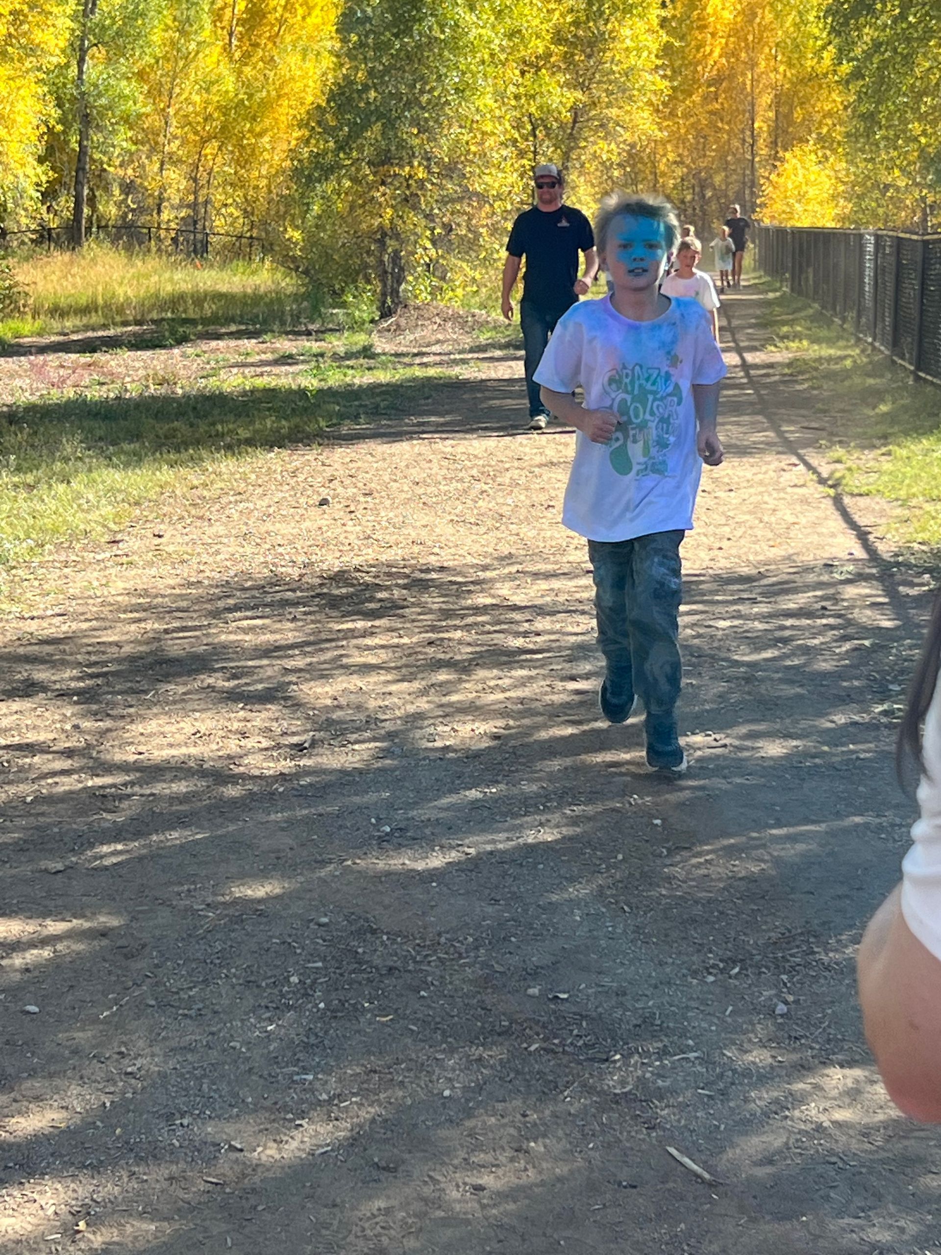 Person running on a dirt path, with yellow trees in the background, another person walking.