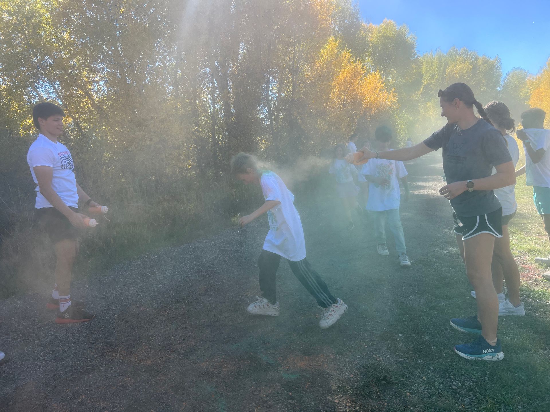 People throwing colored powder. Outdoors, sunny day. One person ducking under a spray of color.