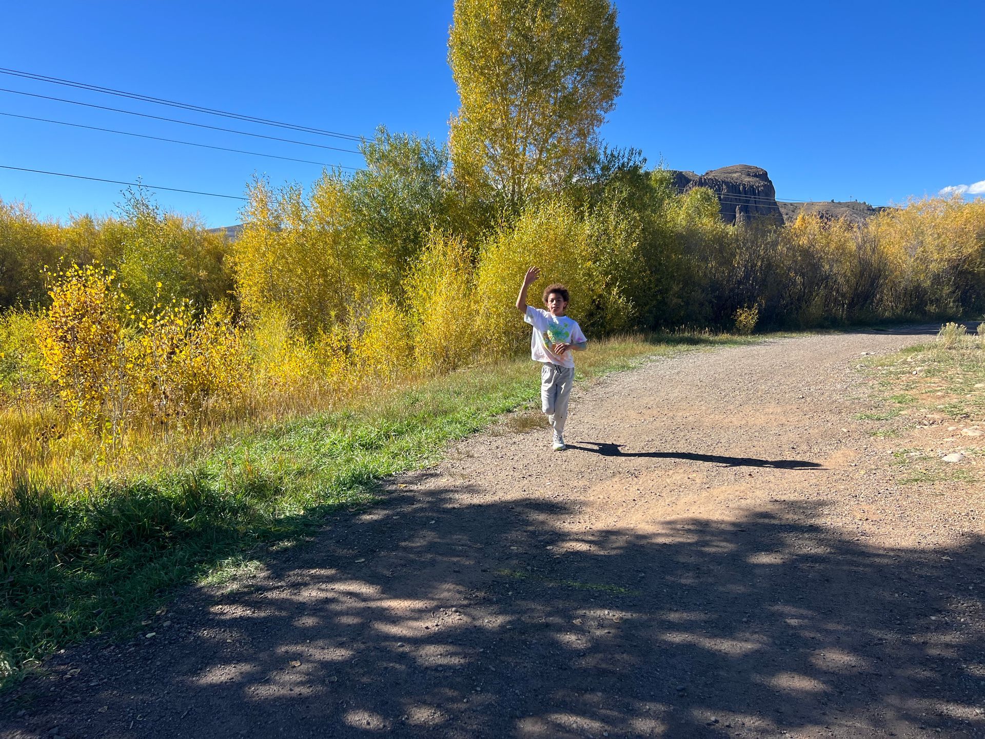 Person running on a dirt path in a sunny, autumn landscape. Yellow foliage and blue sky.