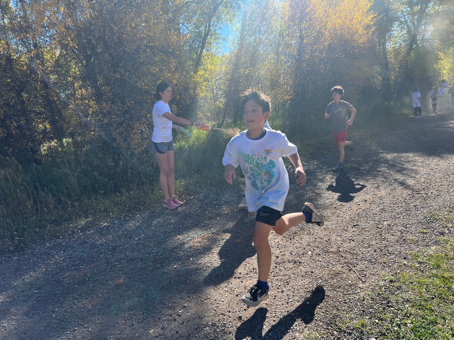 Children running on a gravel path near trees on a sunny day.