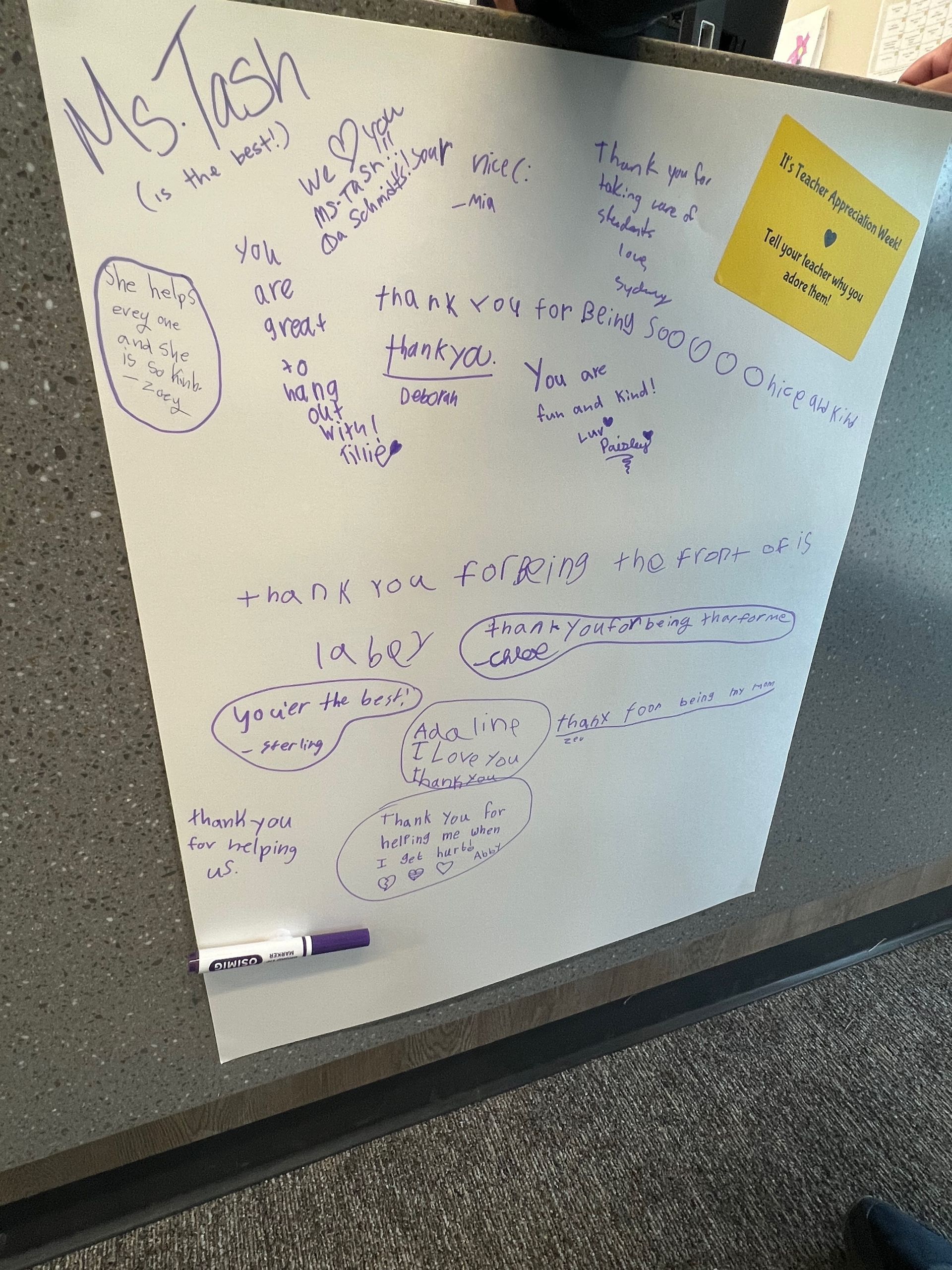 White poster with purple handwriting: calculations and notes. A sticky note is attached. A purple marker is at the bottom.