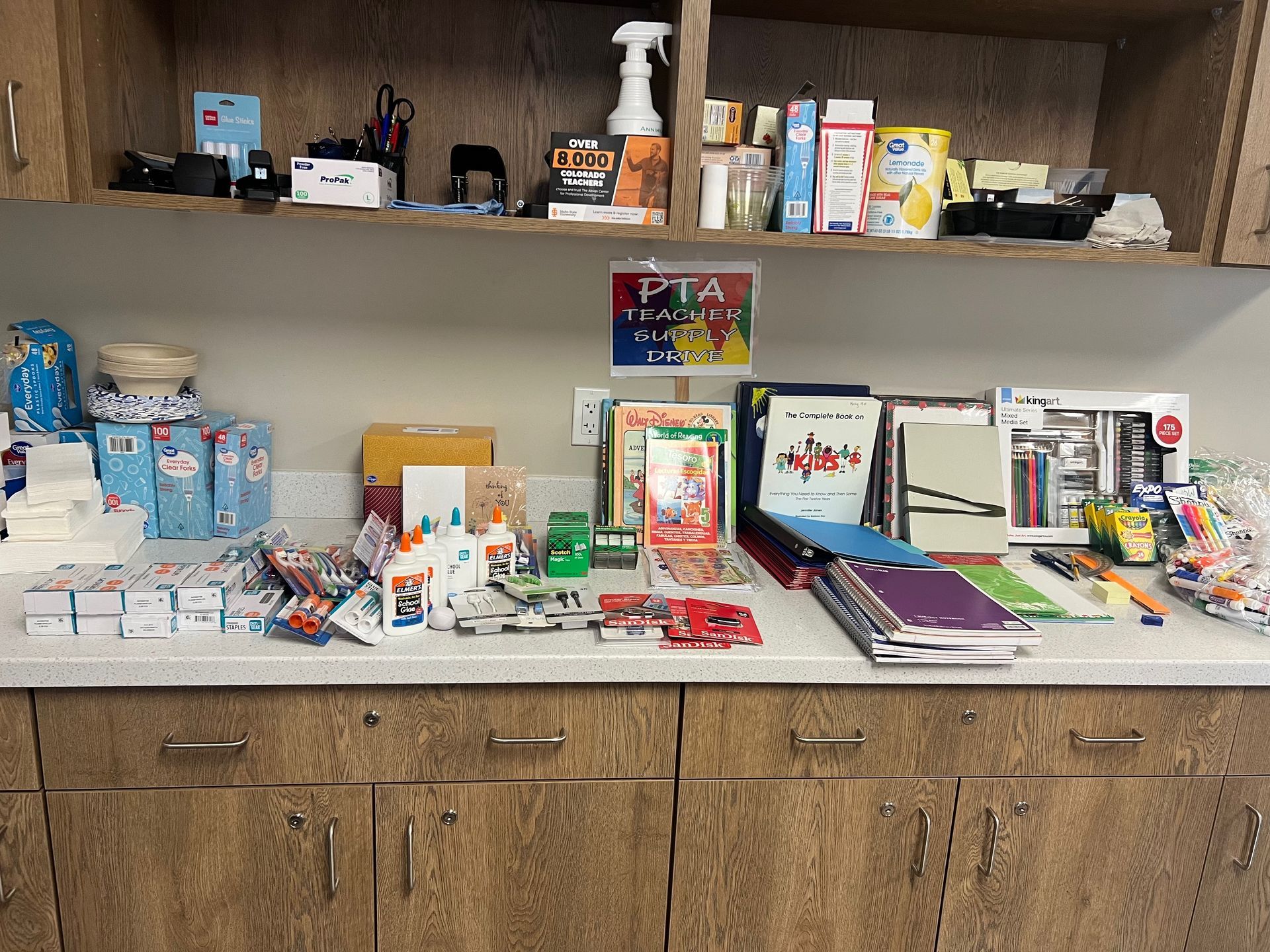 Supplies on a counter, with books, pens, and boxes, likely for a school event, near a PTA sign.