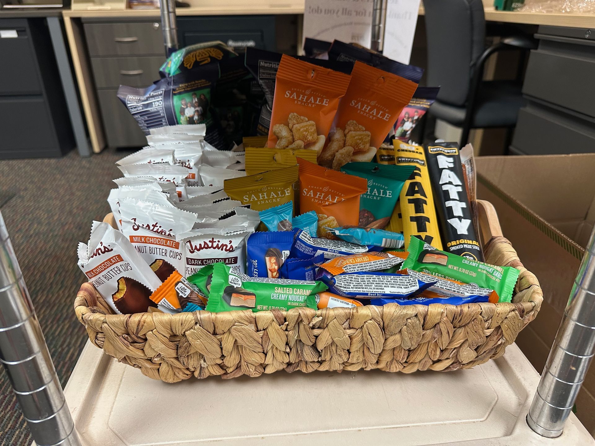 Wicker basket filled with assorted snacks, including bags of nuts, candy bars, and chips.